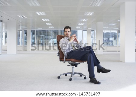 Full length of confident young businessman on chair in empty office space