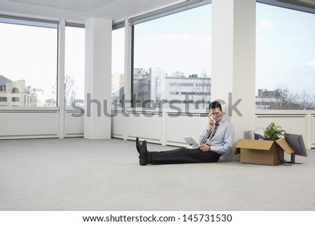 Full length of young businessman using telephone next to cardboard box in new office