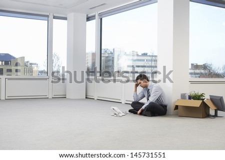 Full length of tensed businessman sitting next to telephone and cardboard box in new office