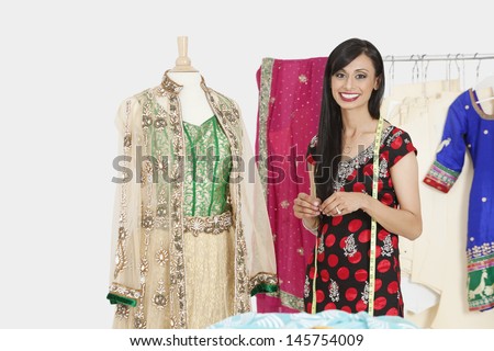 Portrait of Indian female dressmaker standing by a dummy dressed in traditional wear