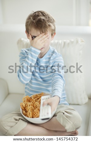 Little boy watching scary movie with a bowl full of wheel shape snack pellets