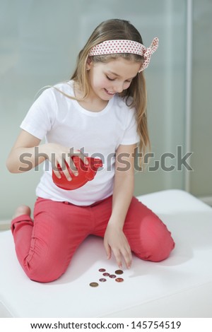 Young girl with piggy bank counting coins on bed