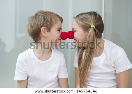 Happy young siblings in white tshirts rubbing clown noses against each other