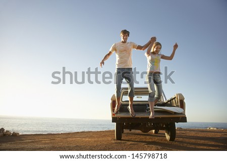 Full length of excited young couple jumping from back of van parked by ocean