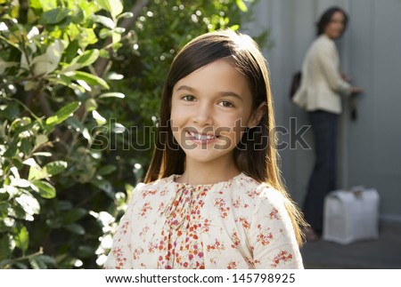 Portrait of young girl smiling in frontyard with mother locking house door