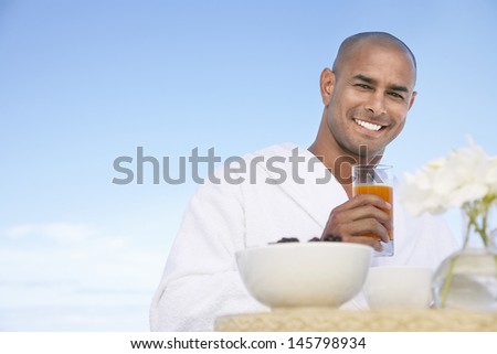 Portrait of happy African American man in bathrobe holding glass of juice outdoors