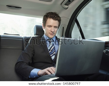 Young businessman using laptop in back seat of car