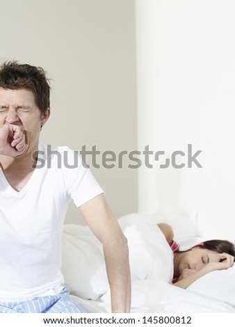 Young man yawning by woman sleeping in bed