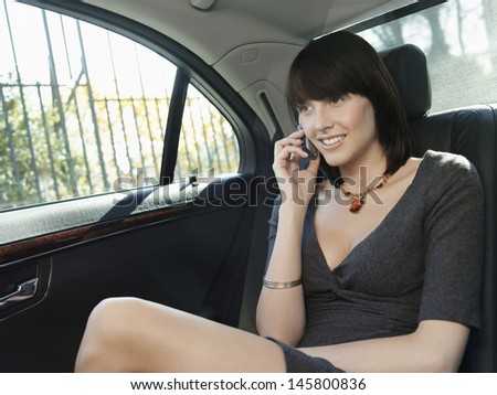 Young businesswoman using cell phone in back seat of car