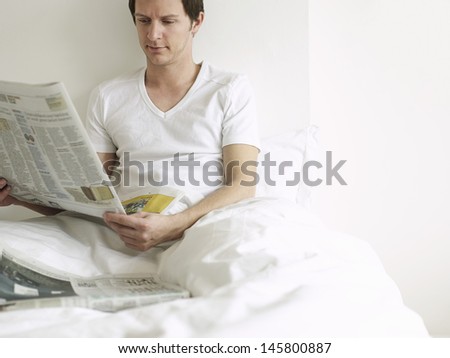 Young man reading newspaper in bed