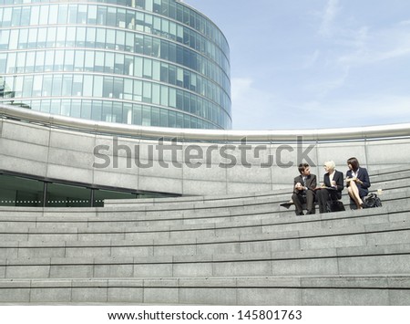 Full length of three business people sitting on steps outside office building during lunch break