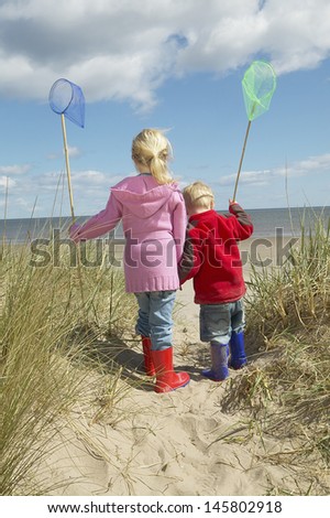 Rear view of brother and sister with fishing nets walking on sand at beach
