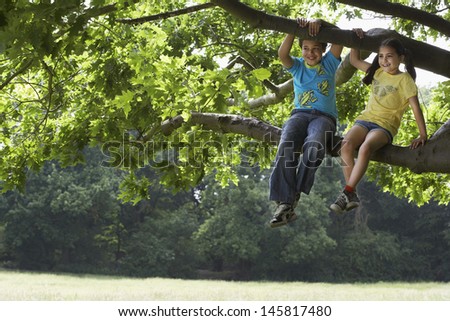 Full length of happy brother and sister relaxing on tree branch