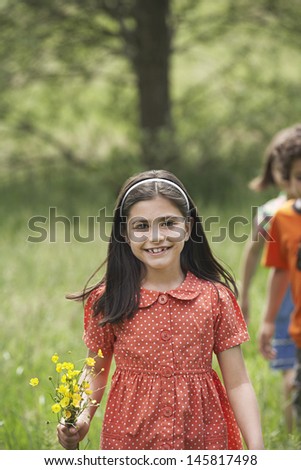Portrait of happy young girl holding bunch of flowers with friends in background at field