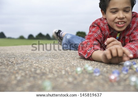 Smiling young boy playing marbles on playground