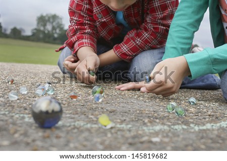 Low section of brother and sister playing marbles on playground