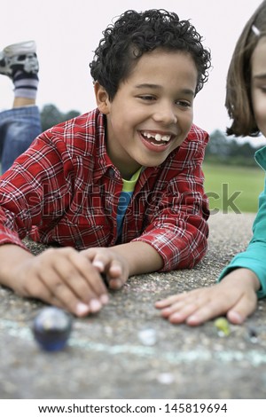 Smiling brother and sister playing marbles on playground