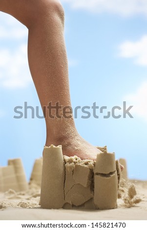 Low section of girl\'s leg stepping on sand castle at beach