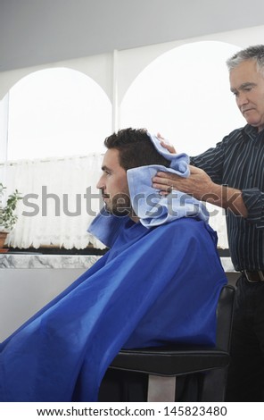 Senior hairdresser drying man\'s hair with towel in barber shop