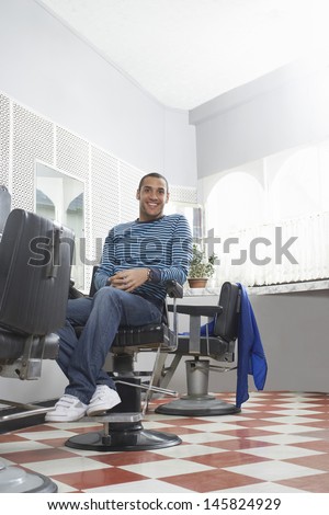 Full length of happy young man sitting on chair in hair salon