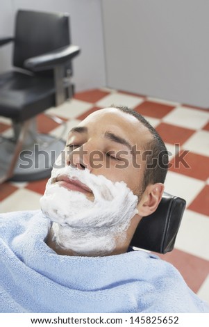 Young man with shaving foam on face resting at barbershop