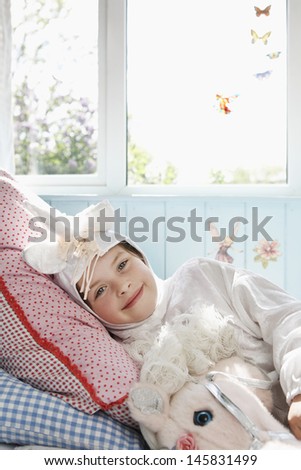 Portrait of a smiling young girl in unicorn costume lying in bed with toy horse