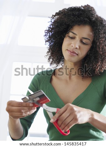 Young mixed race woman cutting credit card against white background