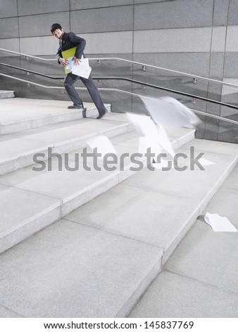 Full length side view of a businessman losing papers from briefcase while walking up steps outdoors
