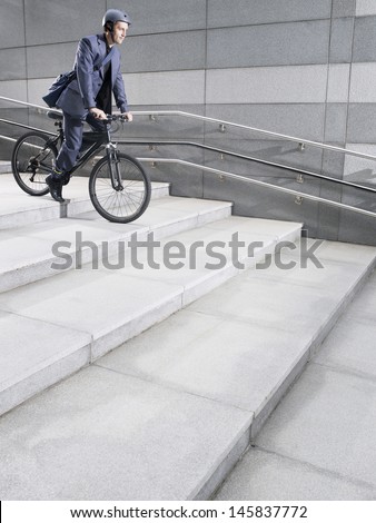 Side view of a businessman in crash helmet riding bicycle down steps