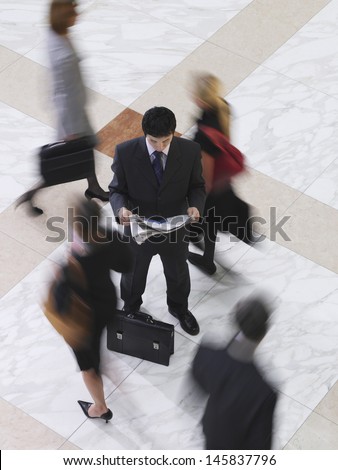 Elevated view of a businessman reading newspaper amongst blurred people walking on tiled floor