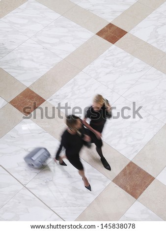 Elevated view of two blurred businesswoman walking with suitcase on tiled floor