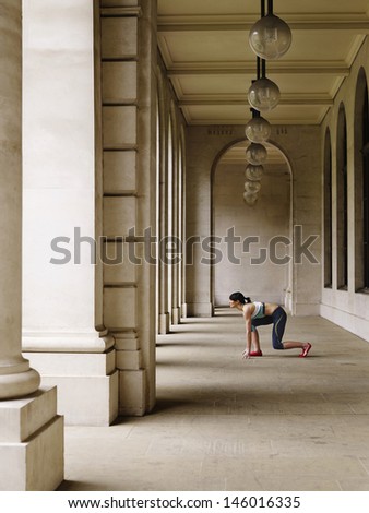 Full length side view of a female runner crouching in starting position in portico