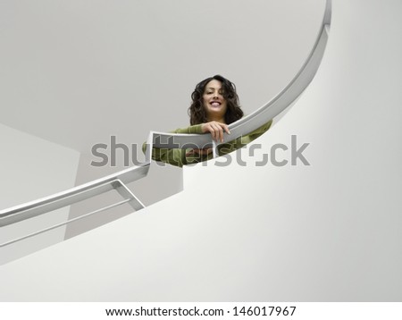 Low angle portrait of a smiling young woman leaning on railing of staircase