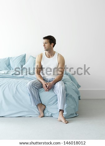 Full length of a thoughtful young man in nightwear sitting in bed