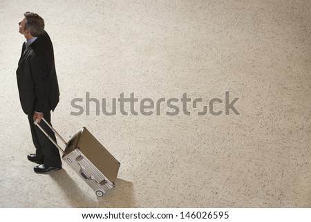 Elevated view of a businessman standing with suitcase in airport lobby