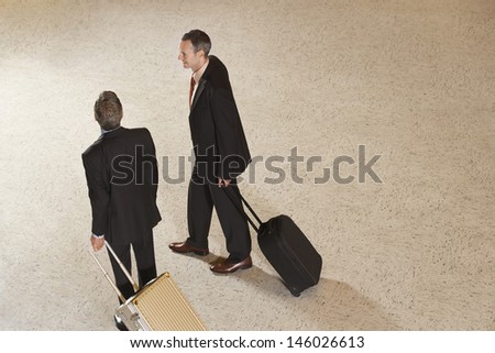 Elevated view of two businessmen pulling suitcases in airport lobby