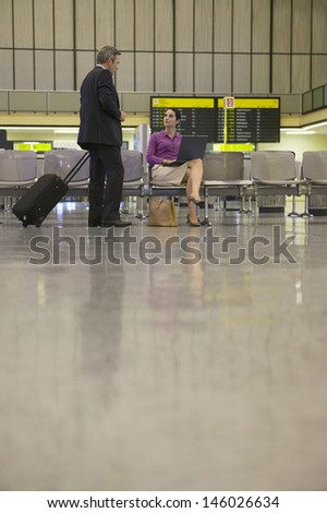 Businesswoman using laptop with businessman approaching her in airport lobby