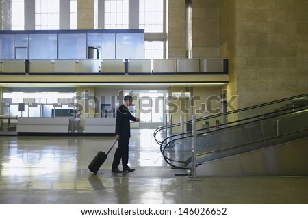 Full length side view of a businessman looking at wristwatch by escalator in airport lobby