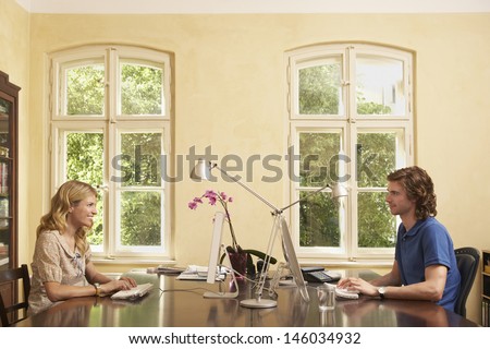 Side view of a young couple using computers across table in study room