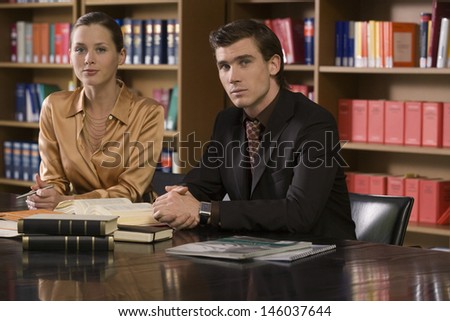 Portrait of a serious young man and woman sitting at desk in the library