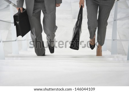 Lowsection of two businesspeople walking up stairs with bags in office