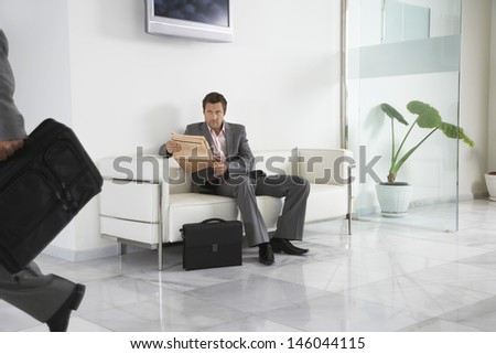 Young man with newspaper looking at cropped person in the office hallway