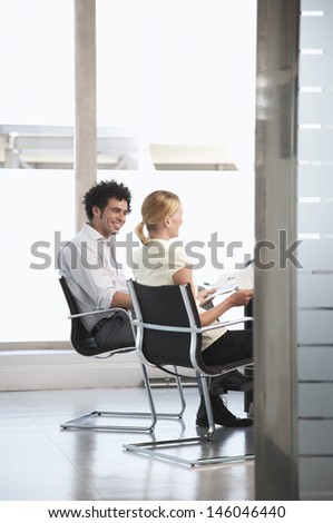 Side view of two happy multiethnic office workers sitting in conference room