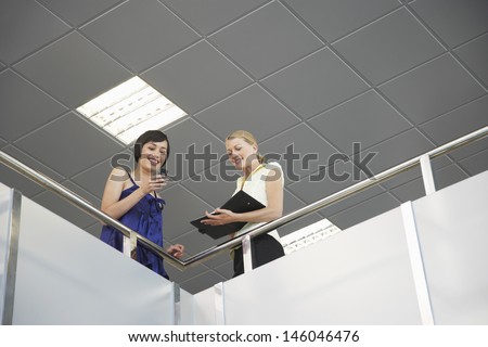 Low angle view of two smiling young business colleagues with cellphone and planner at office balcony