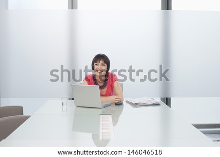 Smiling thoughtful young woman sitting with laptop in modern cubicle at office
