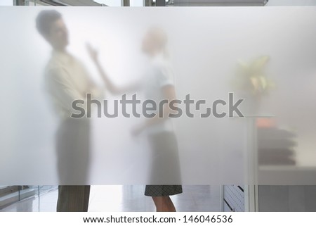Side view of a female office worker arguing with male colleague behind translucent wall in office