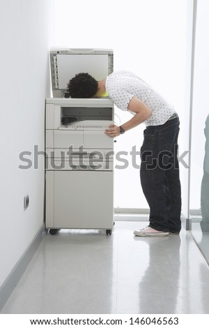 Full length side view of a man putting his head in copy machine in office hallway