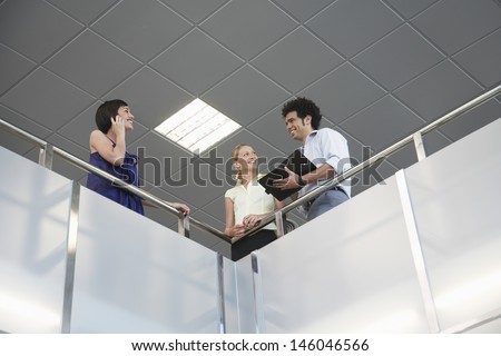 Low angle view of three smiling business colleagues with cellphone and planner at office balcony