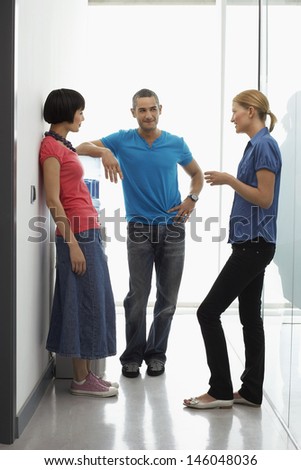 Full length of three office workers talking by water cooler in hallway