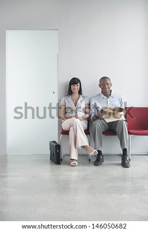 Full length portrait of a young man and woman sitting on chairs in office corridor